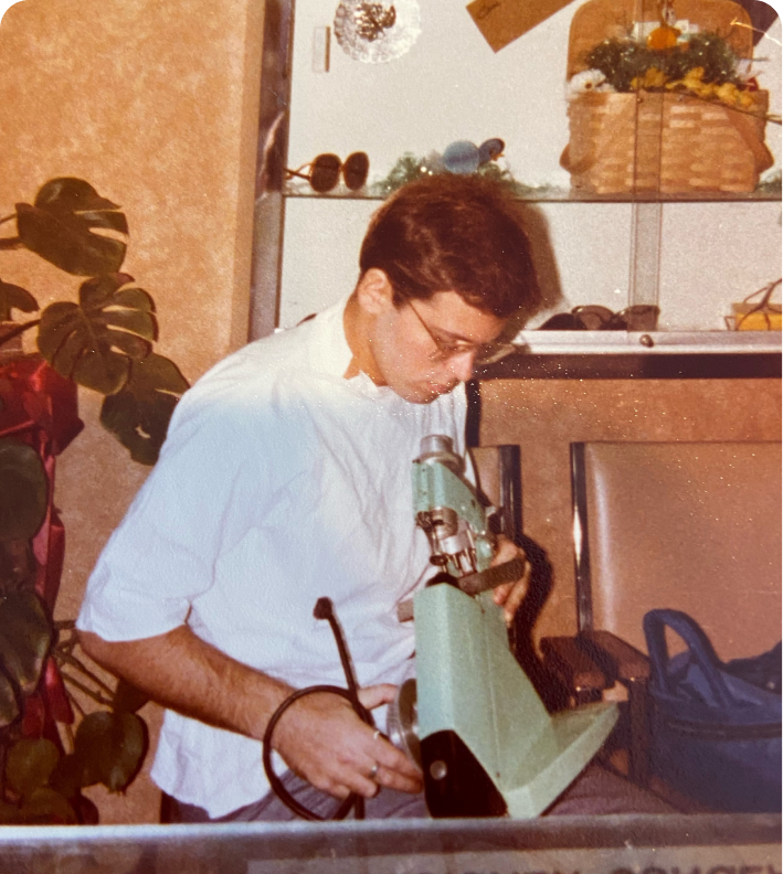 An optician grinding a lens on an edging machine behind the counter of an optical shop.
