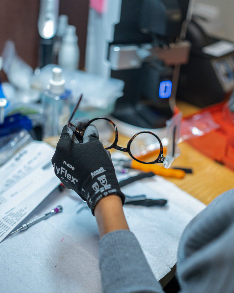 hands holding a pair of glasses over a table with tools and glasses parts